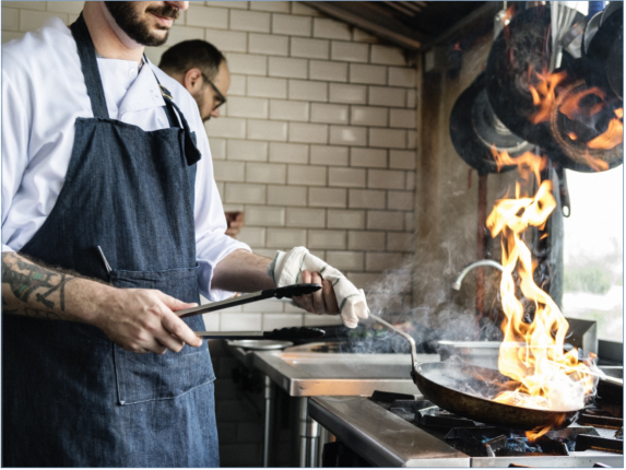 Man cooking food in a skillet pan with flames coming off the pan