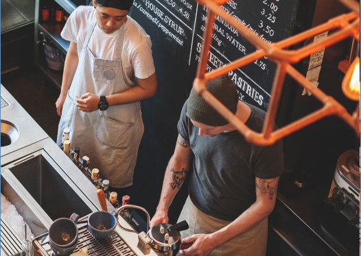 Two restaurant employees standing behind a kitchen counter talking to each other